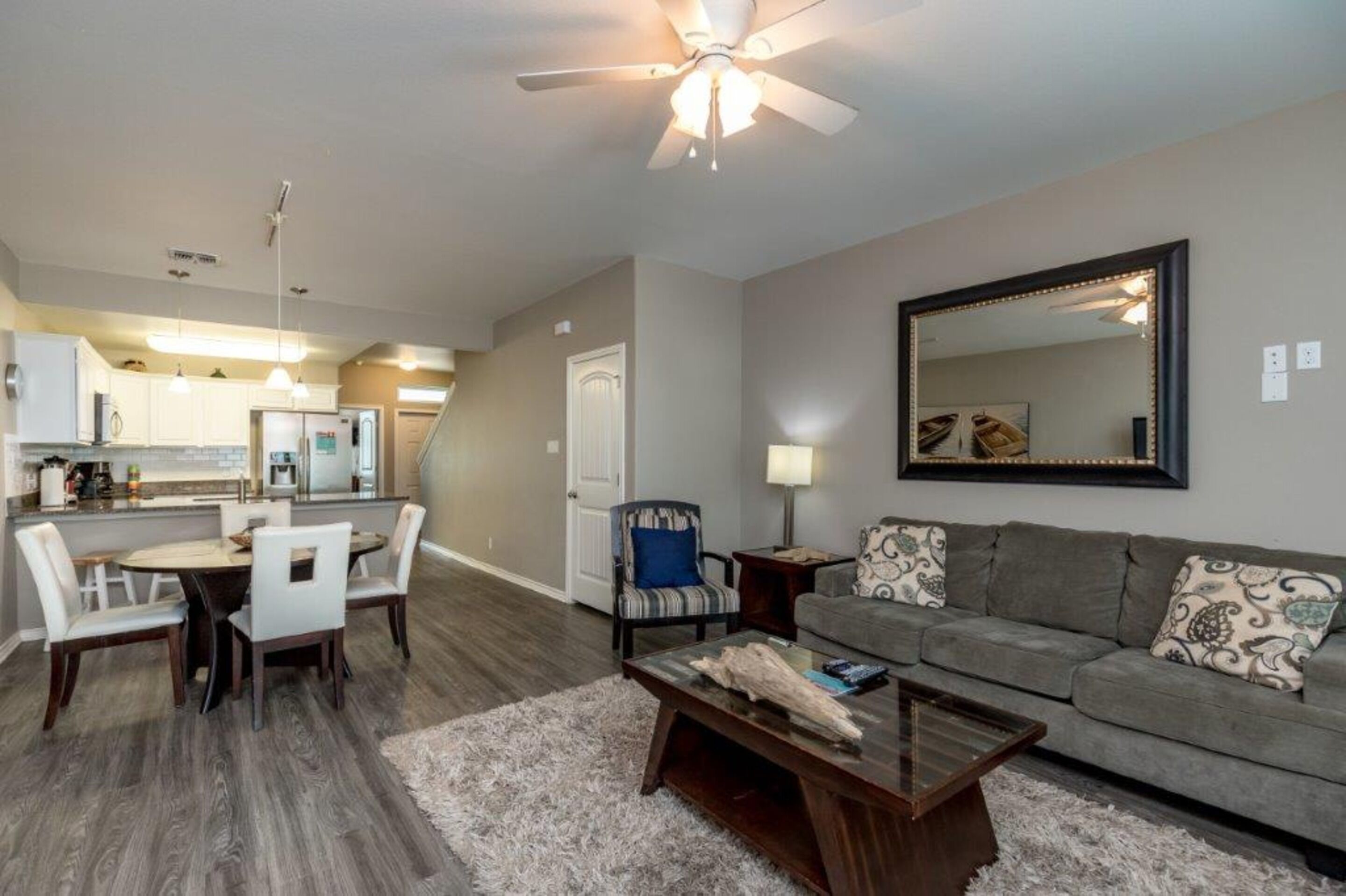 A modern living room with a gray sofa, a coffee table, and a dining area with a white table and chairs.