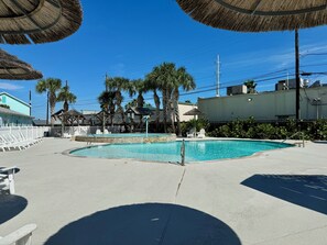 A swimming pool area with a thatched umbrella, white lounge chairs, and palm trees. - Nemo Cay by Silver Sands Vacation Rentals (Corpus Christi)