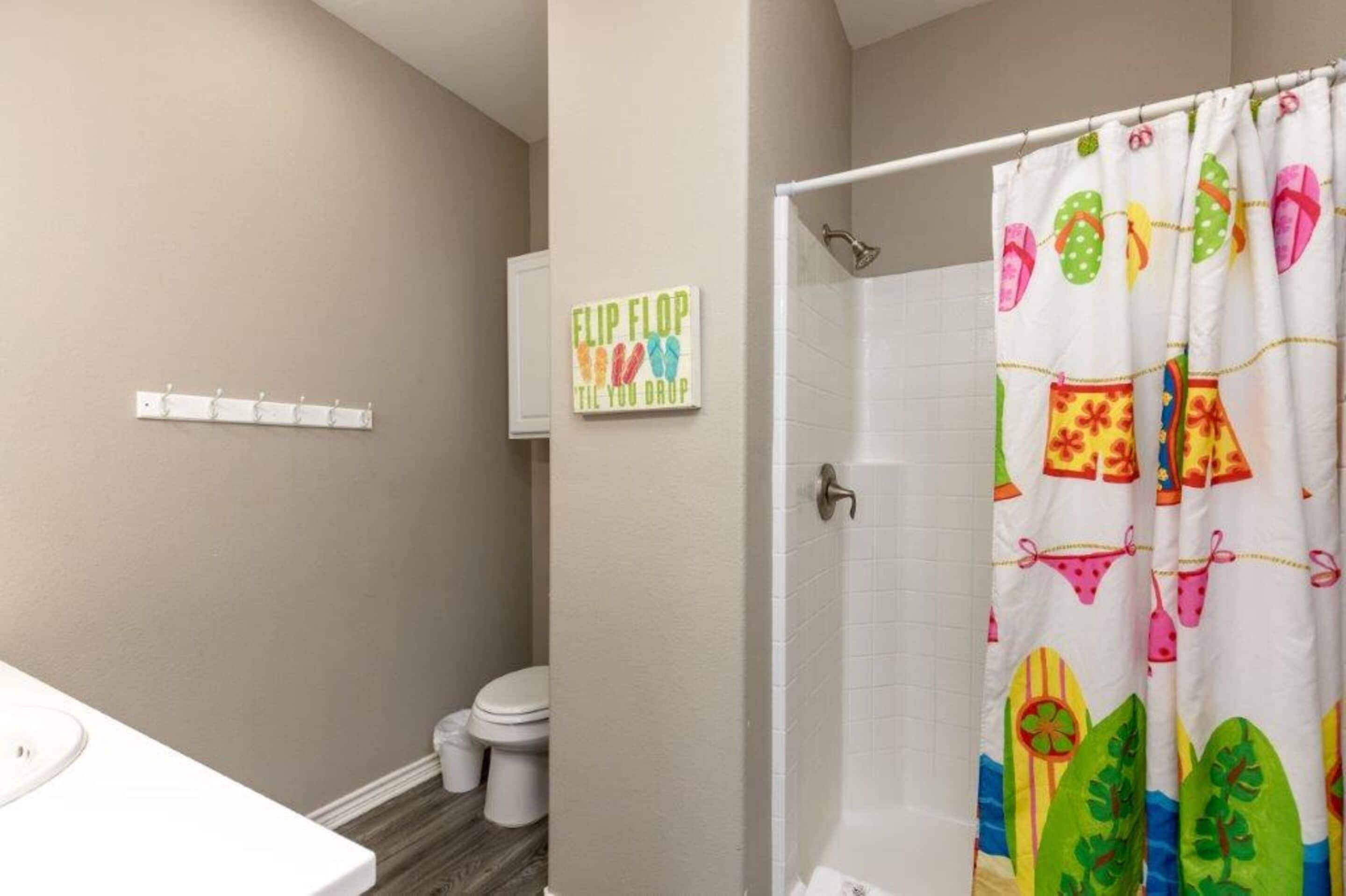 A bathroom with a shower curtain featuring flip flops and beach-themed designs, a toilet, and a wall-mounted towel rack.