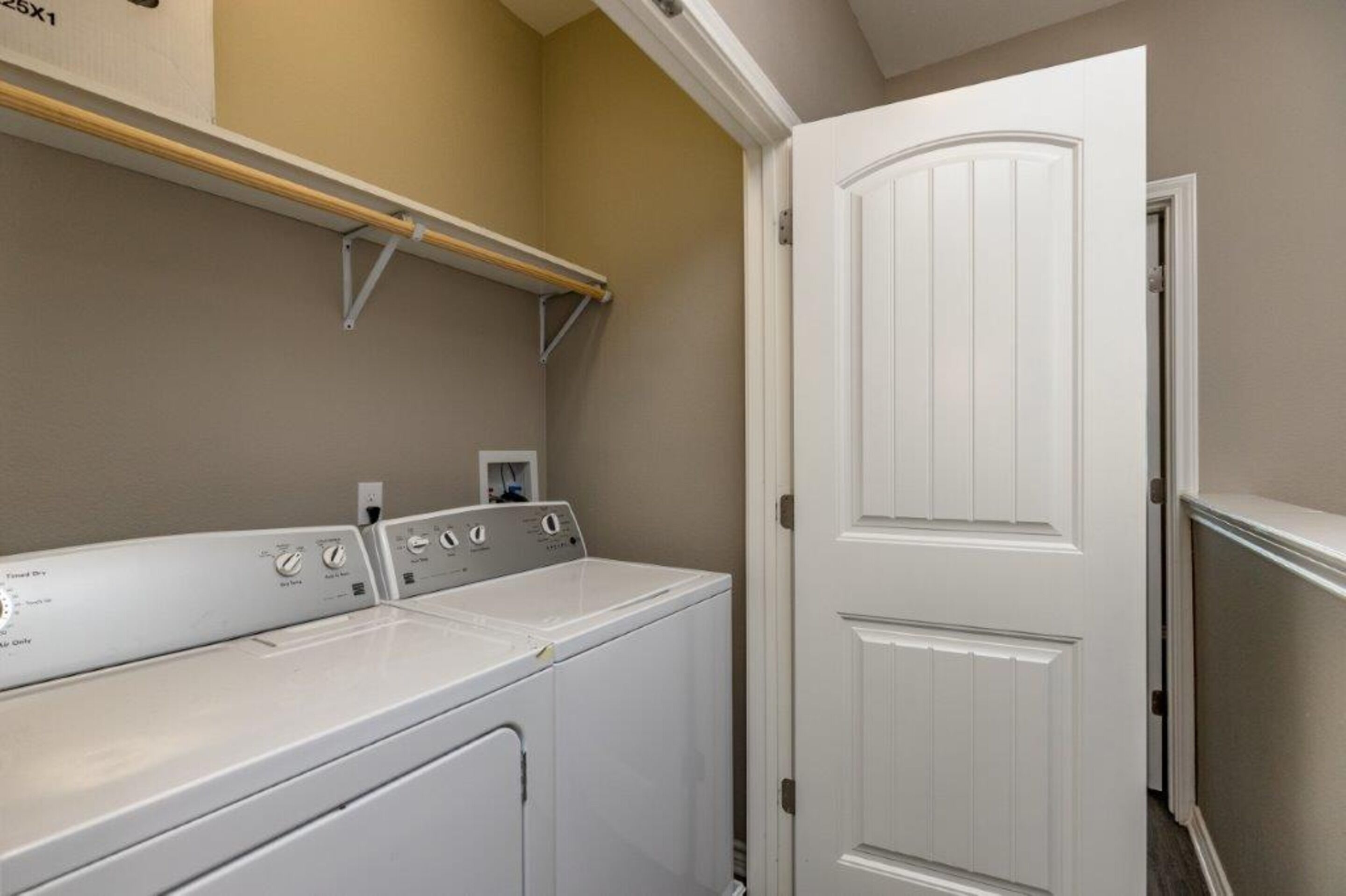 A laundry room with a white wall, a door, and a washing machine.