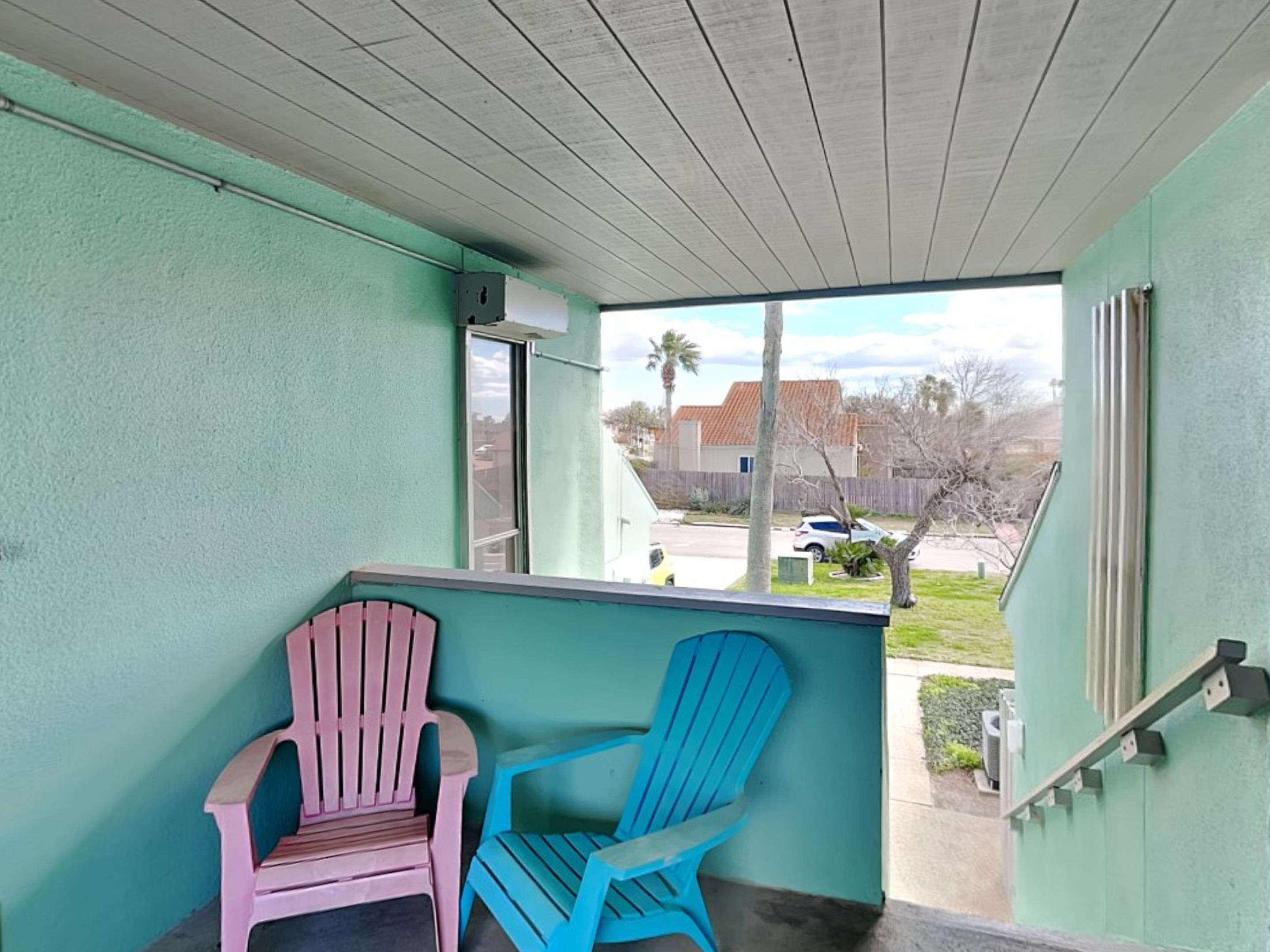 A balcony with two Adirondack chairs, a view of a residential street, and a clear sky.