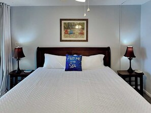 A hotel room with a large bed, two bedside lamps, a framed picture on the wall, and a pillow with text. - Cozy Coastal Repose by Silver Sands Vacation Rentals (Port Aransas)