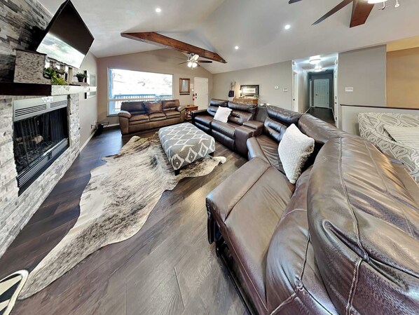 A spacious living room with a fireplace, leather sofas, a large rug, and a ceiling fan. - Blue Sky by Ruidoso Vacation Rentals (Ruidoso)