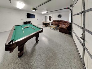A pool table with balls, a sofa, a clock, and a television in a room with a garage door. - Blue Sky by Ruidoso Vacation Rentals (Ruidoso)
