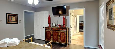 A bedroom with a bed, a ceiling fan, a dresser with red accents, a television, and a door leading to another room.