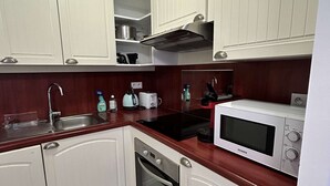 A compact kitchen with white cabinets, a stainless steel sink, a microwave, and a built-in oven. - Pornichet - Résidence Ker Juliette (PORNICHET)