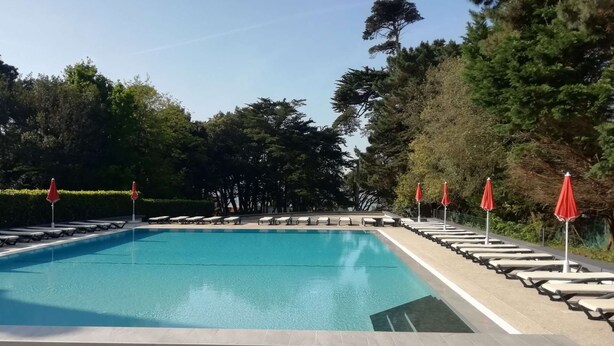 A rectangular swimming pool with a tiled edge, surrounded by lounge chairs and red umbrellas. - Pornichet - Résidence Ker Juliette (PORNICHET)