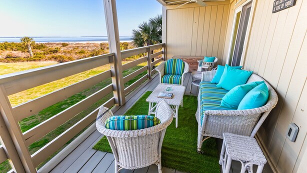Un espacio de estar al aire libre techado con muebles de mimbre, una mesa pequeña y vista a la playa.