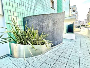 Un bâtiment moderne doté d’un mur incurvé en béton et d’un jardinier contenant de grandes plantes vertes.