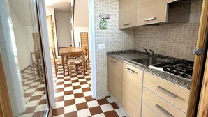 Een keuken met geruit vloerkleed, houten keukenkastjes en een gasfornuis.