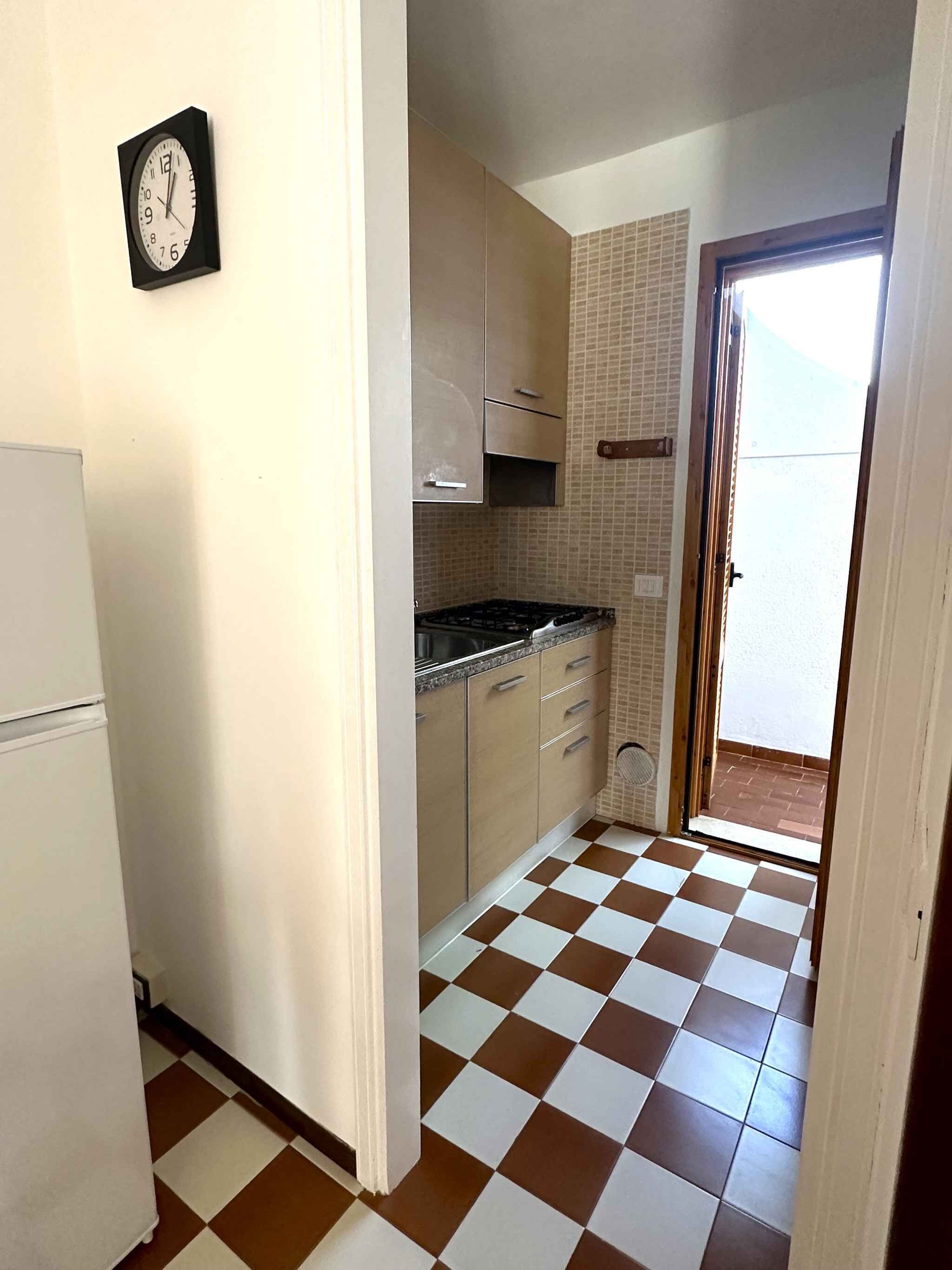 Une cuisine avec un sol carrelé, une cuisinière, des placards et une horloge murale.