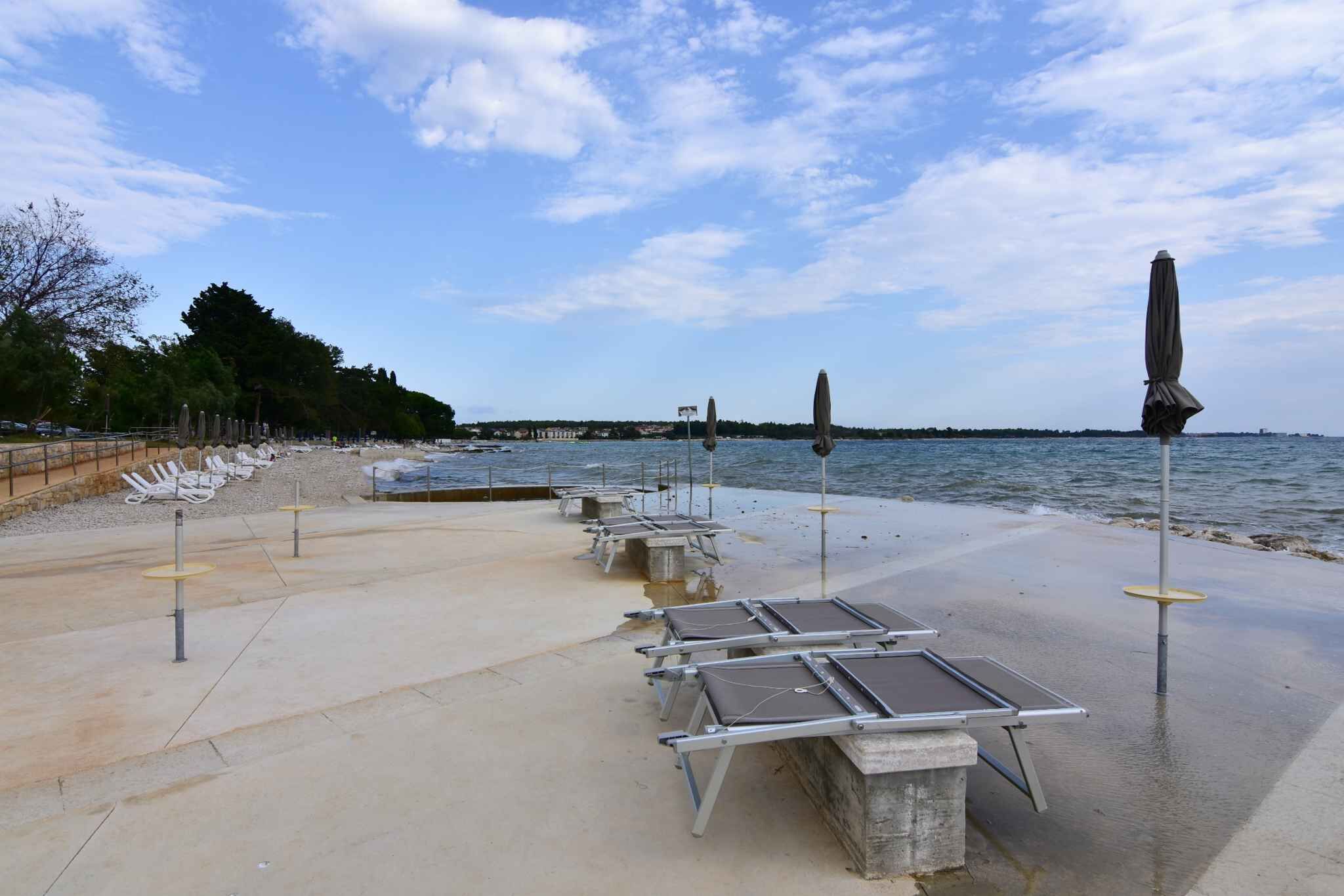 A waterfront promenade with sun loungers and umbrellas, a concrete walkway, and a view of the water.