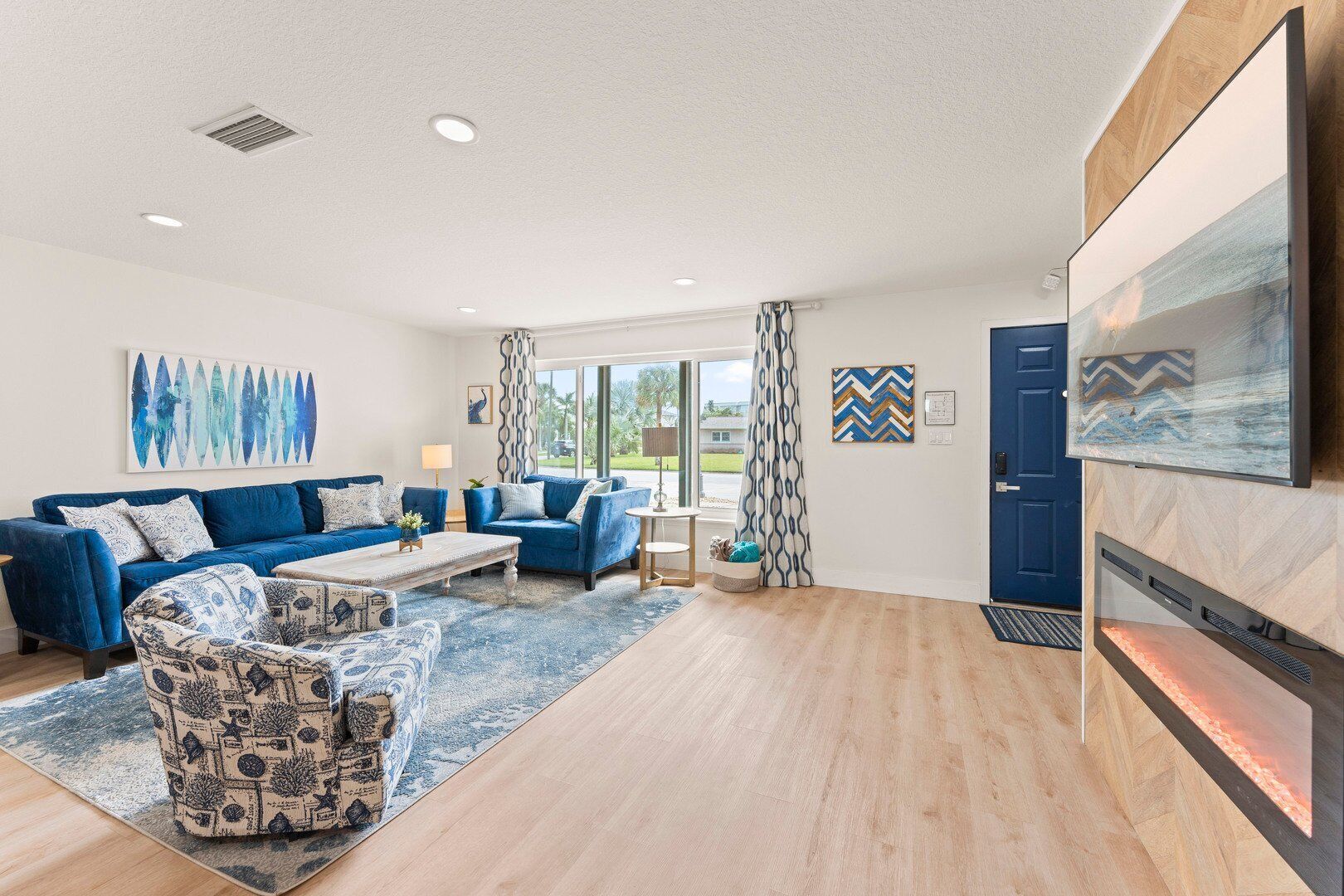 A modern living room with a blue sofa set, patterned armchairs, a coffee table, and a fireplace.