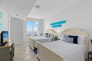 A bedroom with two beds, a TV, and a view of the ocean.