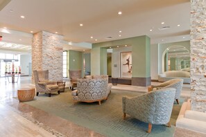 A spacious lobby with multiple seating areas, a stone accent wall, and a large mirror reflecting the space.