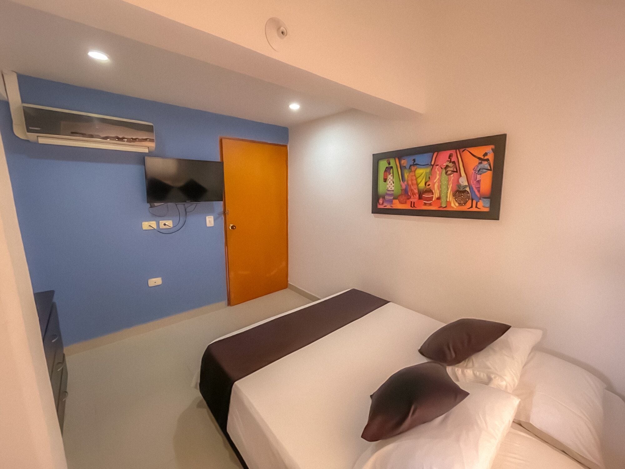 Quarto de hotel com cama, televisão presa na parede e porta.