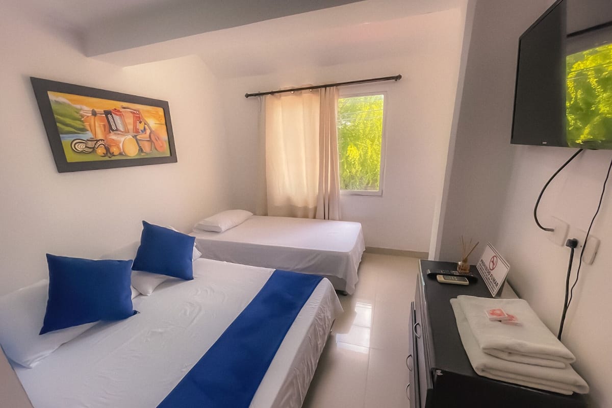 A hotel room with two beds, a TV, a desk, and a window with curtains.