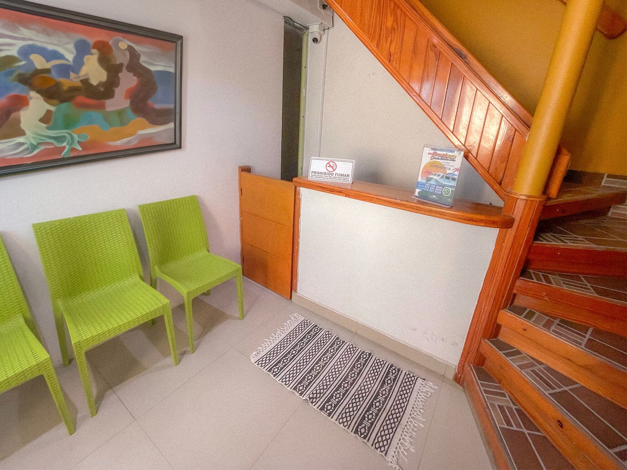 A reception area with a wooden staircase, two green chairs, a patterned rug, and a painting on the wall.
