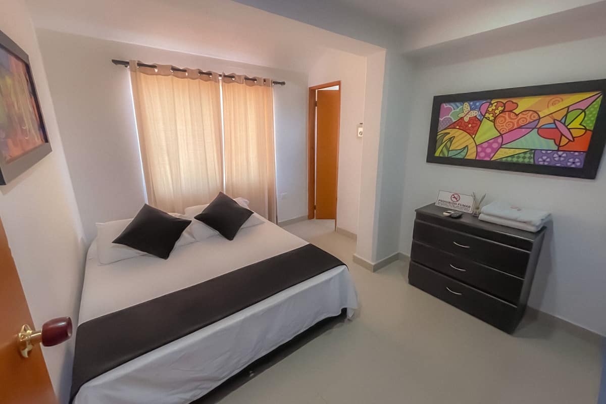 A hotel room with a bed, a dresser, a painting, and a door.