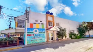 Un hotel llamado "Sweet Caribbean Hotel" con un letrero colorido, una entrada visible y un cielo despejado.