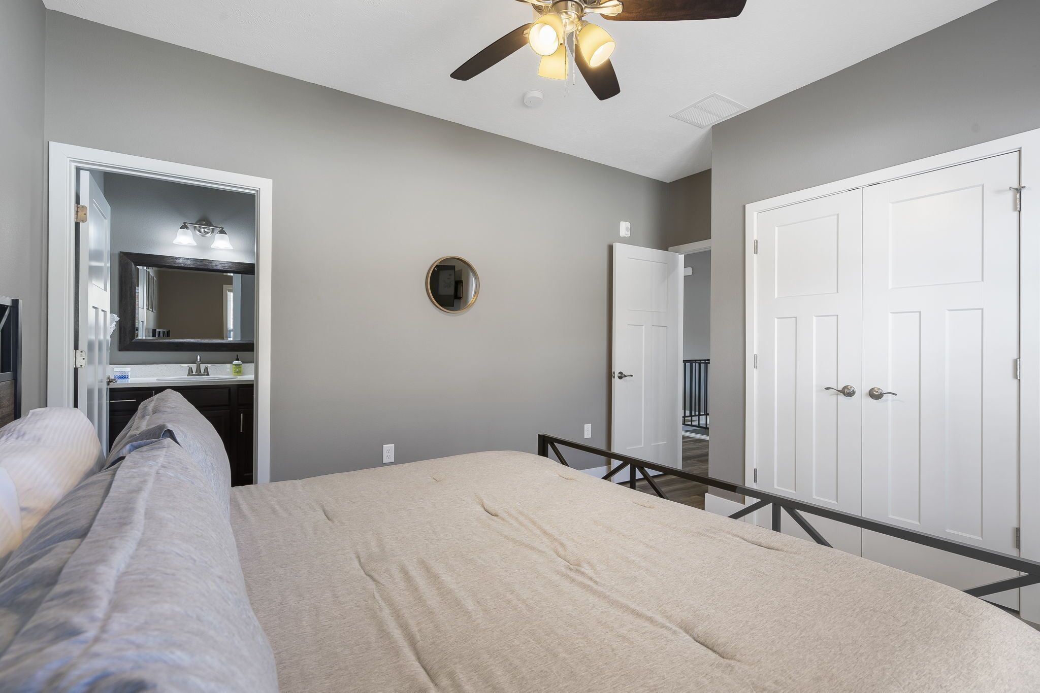 A bedroom with a bed, a ceiling fan, a mirror, a wardrobe, and a door.