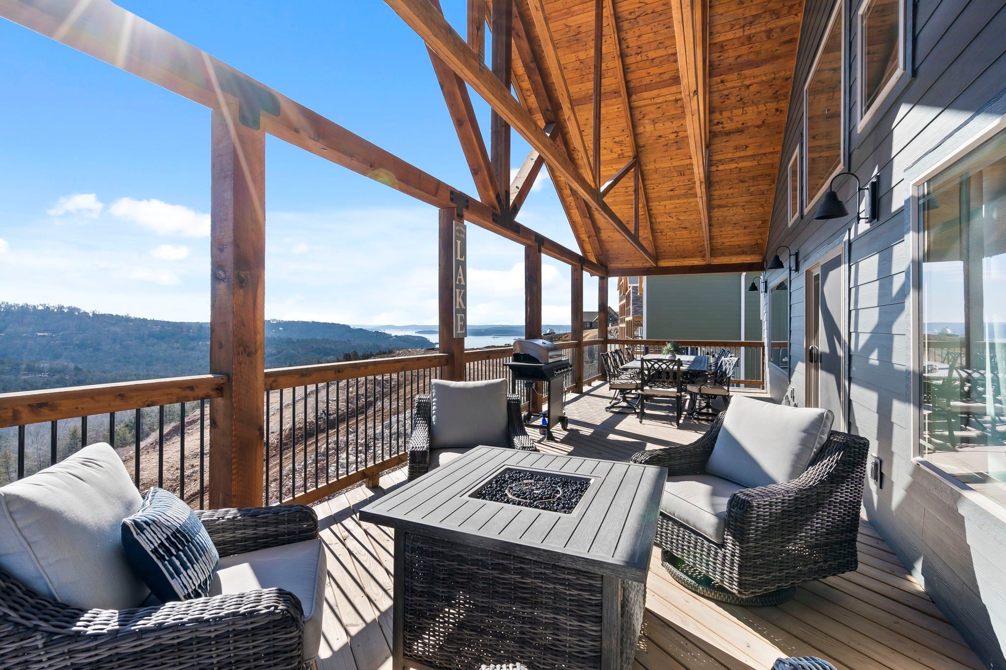 Un terrazzo in legno con mobili da esterno, un barbecue e vista sul lago.