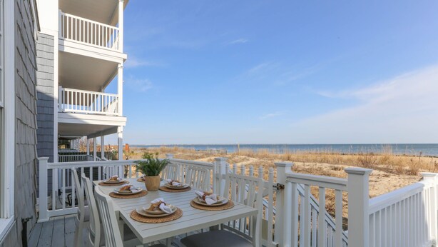 A white deck with a table set for four, overlooking a beach with sand dunes. - Waterfront Willoughby Oasis (Norfolk)