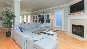 A spacious living room with a sectional sofa, a fireplace, and a television mounted above it. - Waterfront Willoughby Oasis (Norfolk)