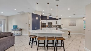 Uma cozinha moderna com uma ilha grande, armários brancos e iluminação pendente.