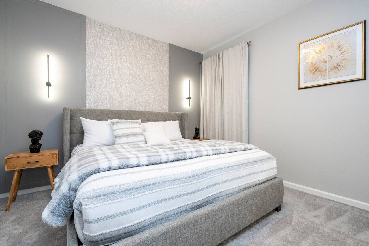 Een moderne slaapkamer met een groot bed, een nachtkastje, een wandlamp en een lijst met een kunstwerk.
