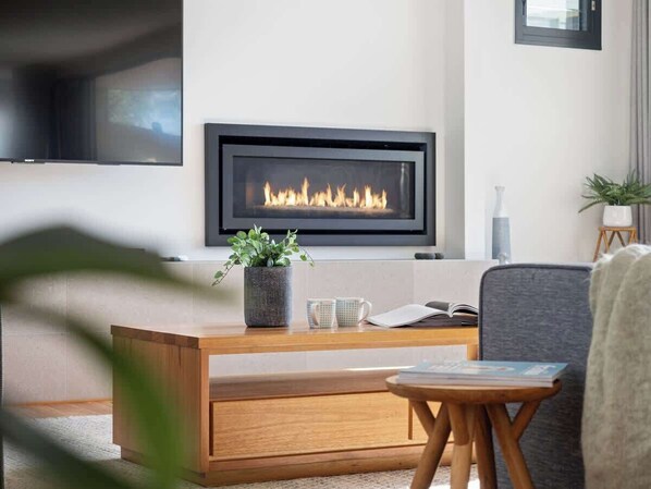 A modern living room with a fireplace, a coffee table, a sofa, and a TV mounted on the wall.