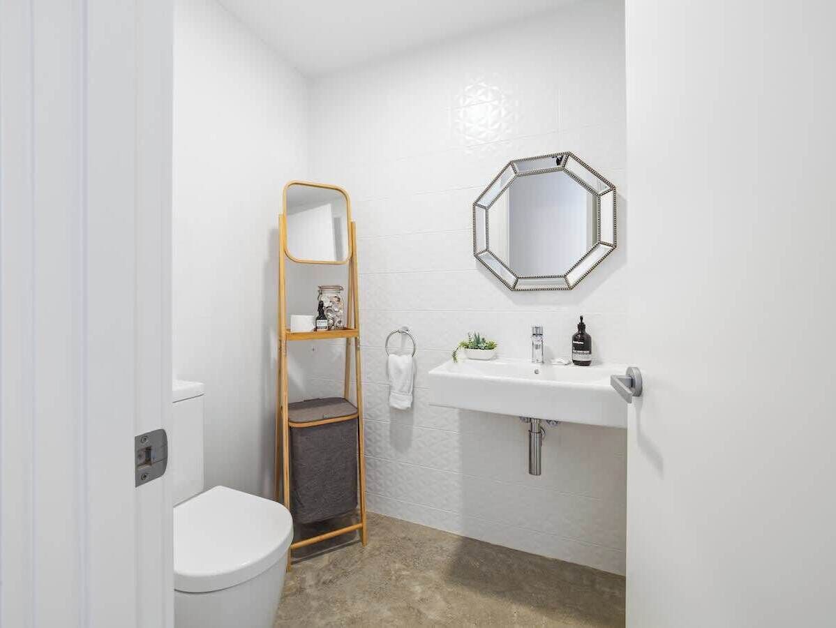 A small bathroom with a toilet, a wooden shelf, a sink with a mirror, and a towel rack.