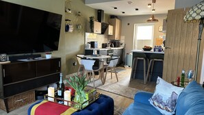 Un salon moderne avec un téléviseur à écran plat, un canapé bleu et un coin repas avec une cuisine en arrière-plan.