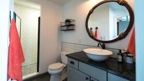 Un baño con inodoro blanco, un lavabo con espejo redondo y zona de ducha.
