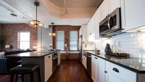 Una cocina moderna con armarios blancos, un microondas de acero inoxidable y piso de madera.