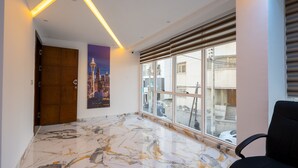 A modern hallway with a marble floor, a wooden door, a large window with blinds, and a poster of a cityscape. - Immoka Apart-hotel (Tangier)