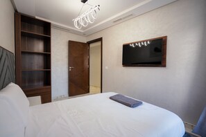 A bedroom with a bed, a wooden wardrobe, a television mounted on the wall, and a ceiling light fixture. - Immoka Apart-hotel (Tangier)