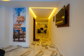 A hallway with a marble floor, a wall-mounted TV, and a painting of a Mediterranean scene. - Immoka Apart-hotel (Tangier)