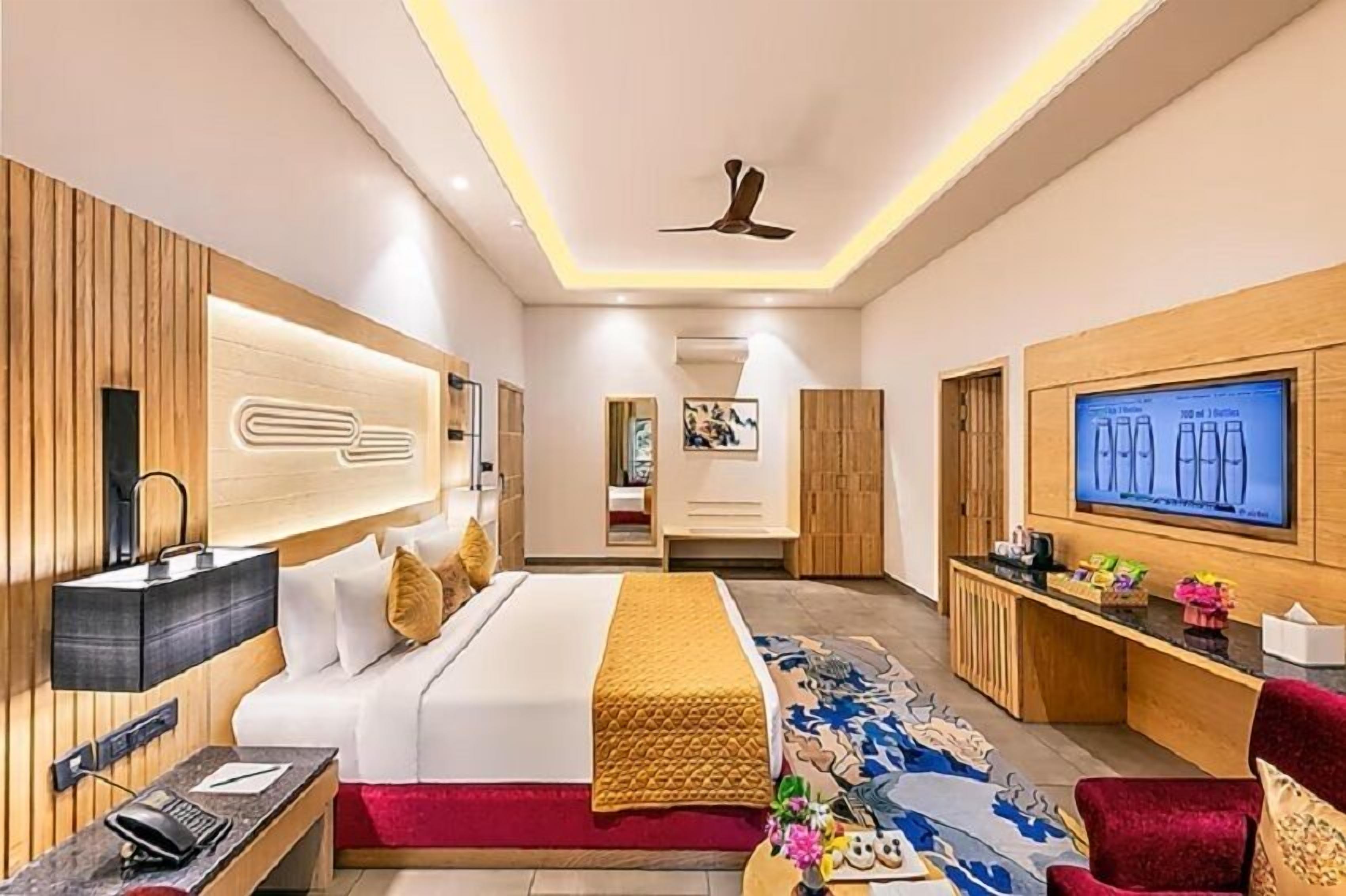 Ein modernes Hotelzimmer mit Bett, Schreibtisch, Fernseher und Deckenventilator.