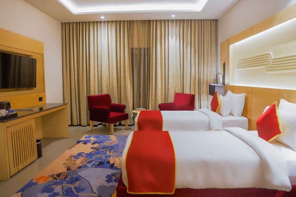 A hotel room with two beds, a desk, a television, and a red chair.