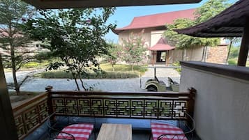 A balcony with a checkered bench and a table, overlooking a courtyard with a building and trees.