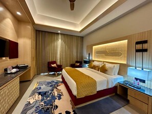 A hotel room with a large bed, a desk, a chair, a television, and a decorative wall panel. - Ananta Spa & Resorts Jaipur (Jamwa Ramgarh)