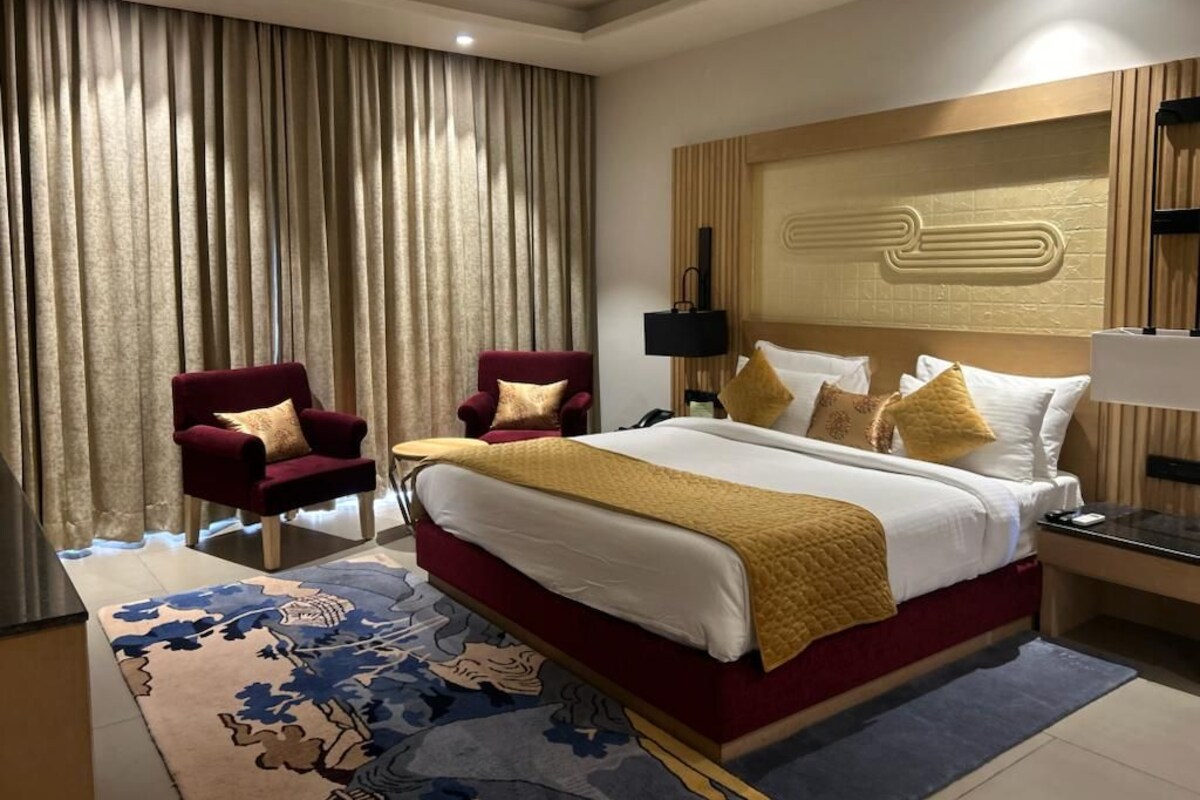A hotel room with a large bed, two armchairs, a nightstand, and a decorative headboard.