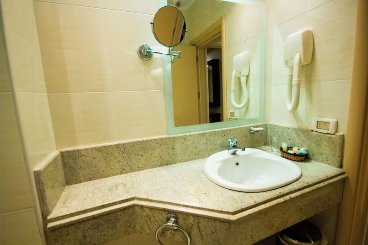 A bathroom with a granite countertop, a white sink, a mirror, a handheld showerhead, and a towel rack.