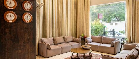 A living room with a sectional sofa, a coffee table, and a wall clock displaying time from four different countries.