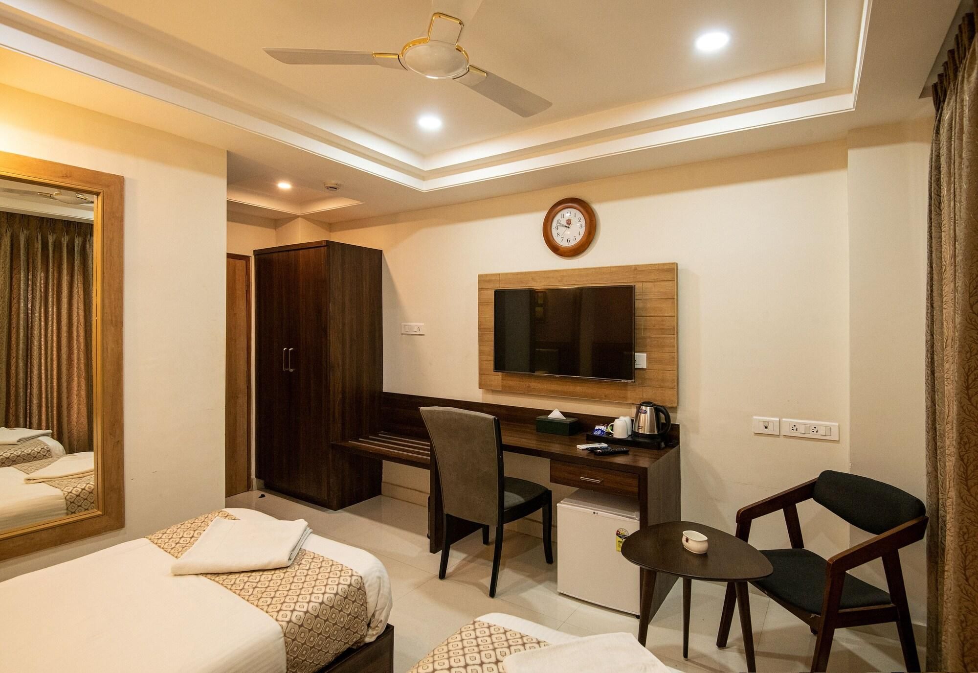 A hotel room with two beds, a desk, a chair, a small table, a television, and a clock on the wall.