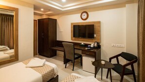A hotel room with two beds, a desk, a chair, a small table, a television, and a clock on the wall.