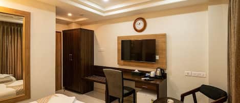 A hotel room with two beds, a desk, a chair, a small table, a television, and a clock on the wall.