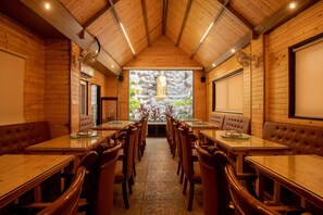 Restaurante com interior em madeira, várias mesas e cabines, e uma grande janela com vista para o verde.