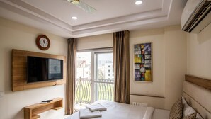 A hotel room with a bed, a mounted TV, a painting, and a balcony with curtains. - M Square Hotel-hitec City (Hyderabad)